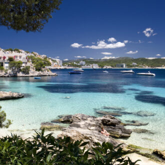 Cala Fornells cove with turquoise water, rocky terraces, and swimmers in Mallorca.