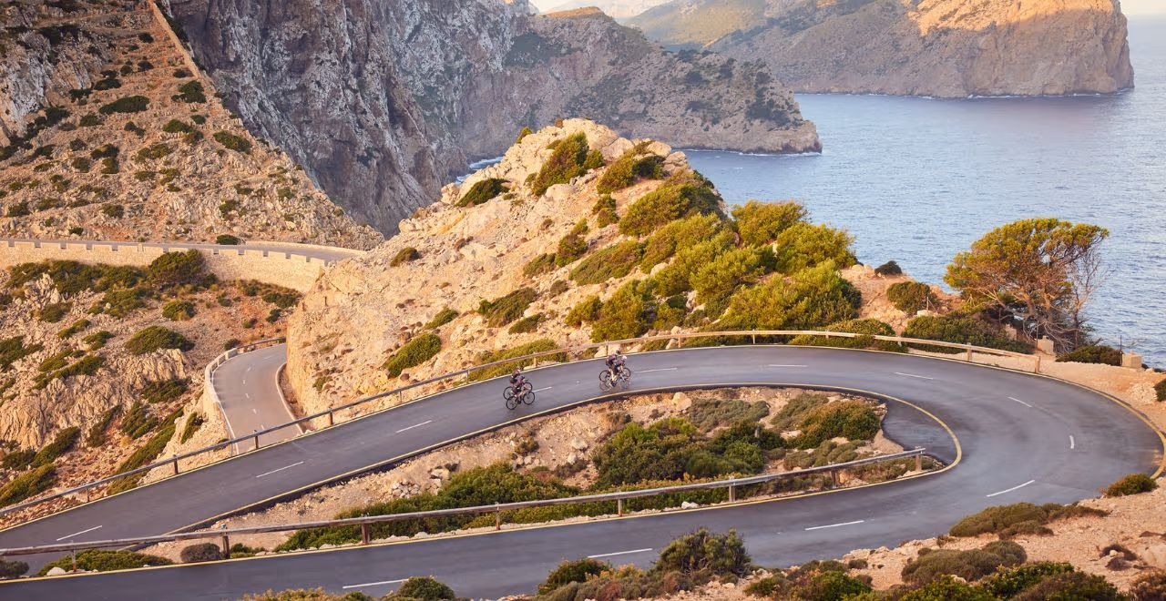 Cyclist riding along coastal road towards Cap de Formentor lighthouse in Mallorca.